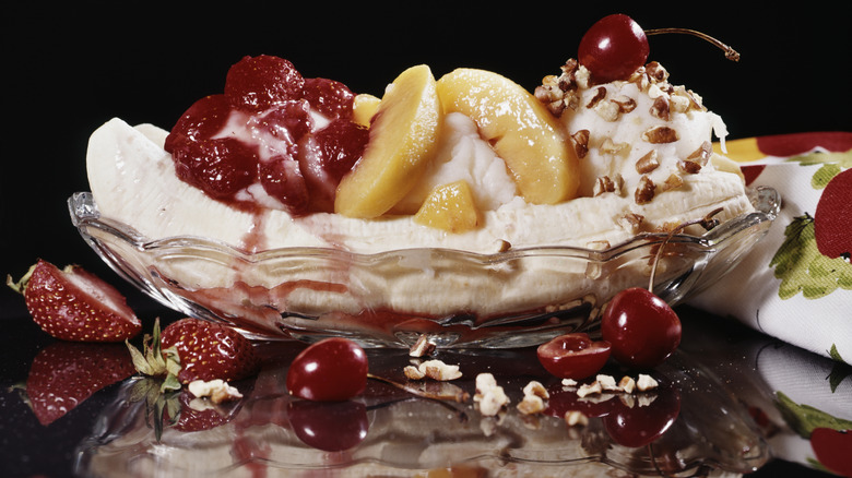 A vintage image of a banana split with fruit, nuts, cream, and a cherry on top