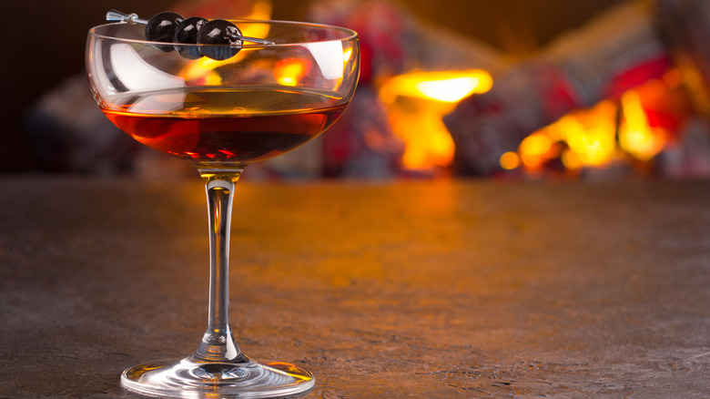Glass of Manhattan sits in front of fireplace.