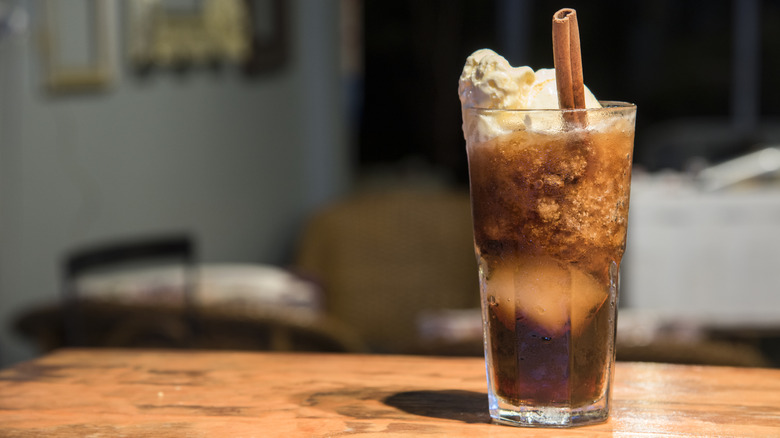 Root beer float served on a table with a cinnamon stick straw.