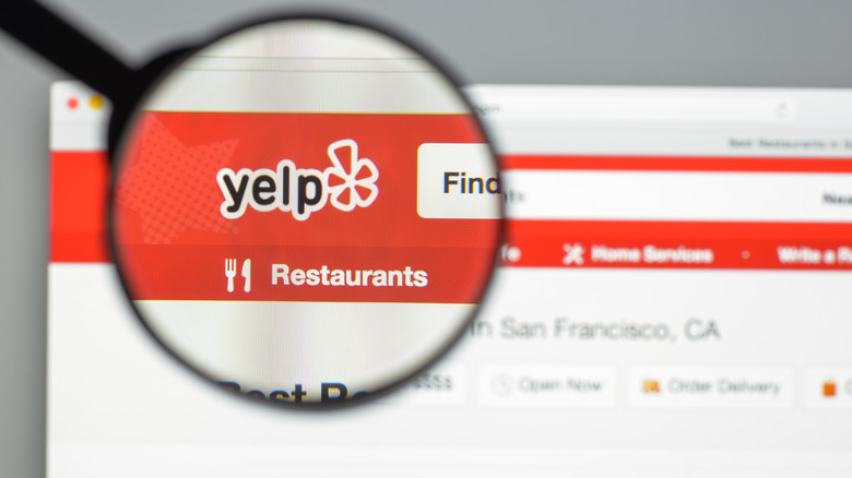 Someone holds up a magnifying glass to Yelp's website, highlighting the logo.