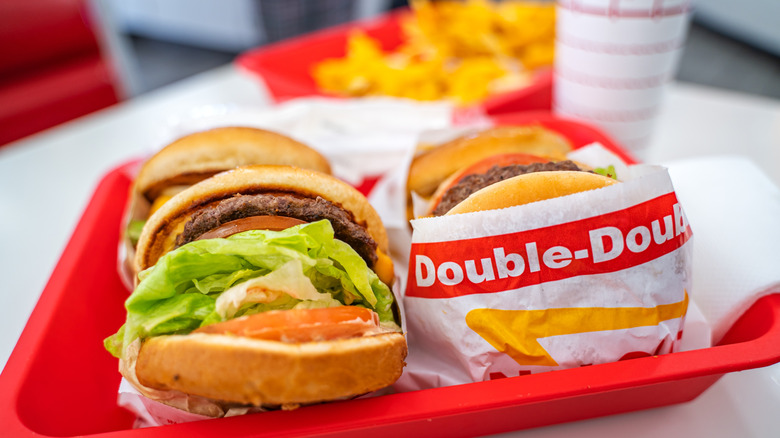 An In-N-Out Double-Double burgers sit on a red restaurant tray in front of fries and a drink in its classic palm-tree cup