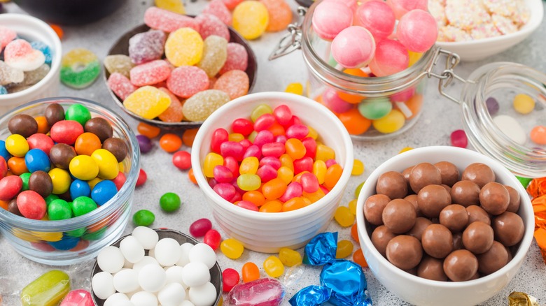 Candies in small white ramekins and glass jars including jelly beans, chocolate balls, and gummies