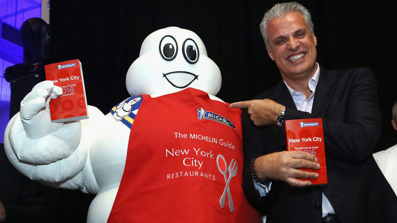 Chef Eric Ripert with the Michelin Tires Michelin Man mascot in a red apron holding Michelin Guides for New York City