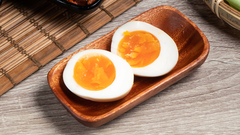 Two halves of a soft-boiled egg in a small wooden tray