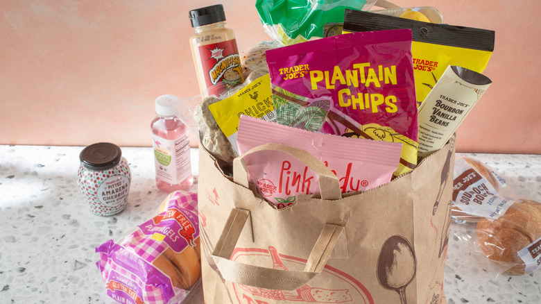 A Trader Joe's shopping bag filled with different snacks, chips, bagels, and other popular items