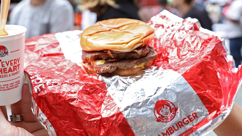 A hand holds a Wendy's Baconator aloft on its wrapper