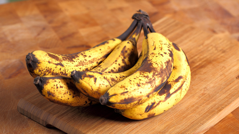 Overripe bananas sitting in a bunch on a wooden counter