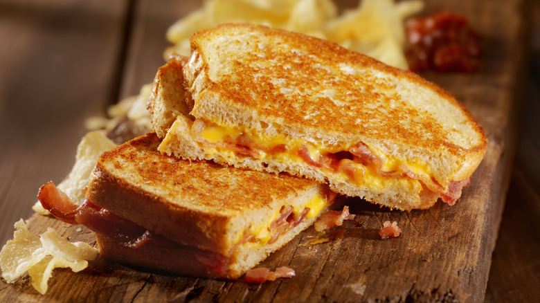 bacon grilled cheese on a wooden plank with potato chips in the background