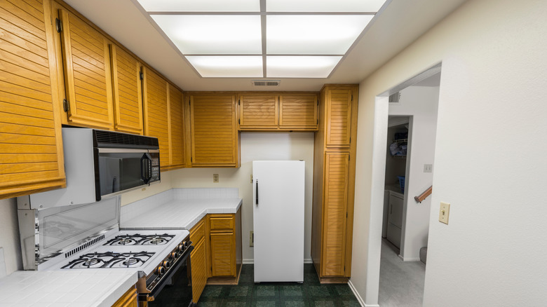 A retro 1980s kitchen with wood-paneled cabinets and a drop ceiling containing fluorescent lighting