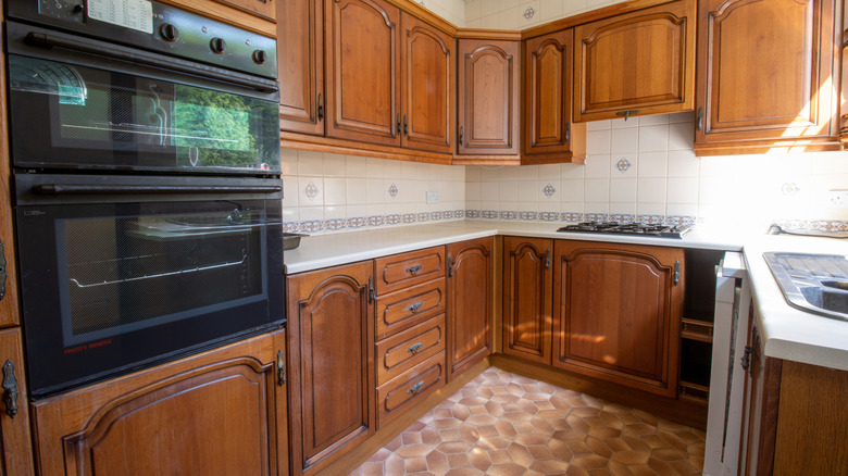 A 1980s kitchen with old-school honey oak cabinetry, a tile backsplash, and a linoleum floor