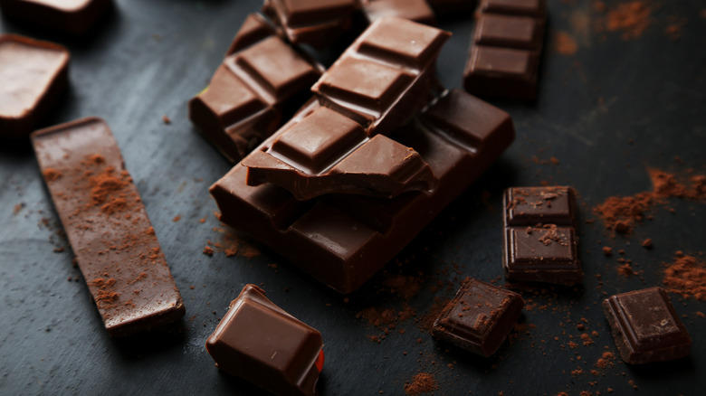 A thick chocolate bar sits broken and dusted with cocoa powder