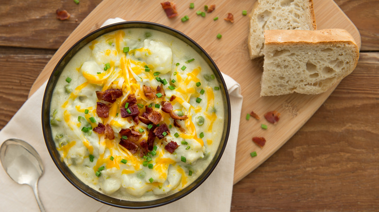 a bowl of chunky potato soup topped with bacon, chives, and cheese next to sourdough