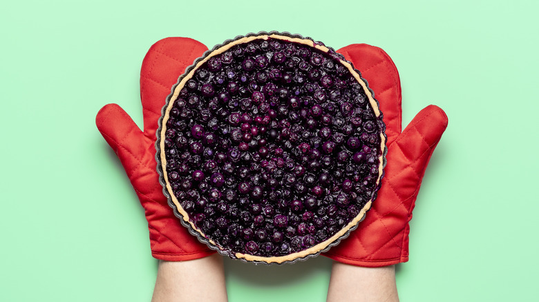 Person with oven mitts holding blueberry pie