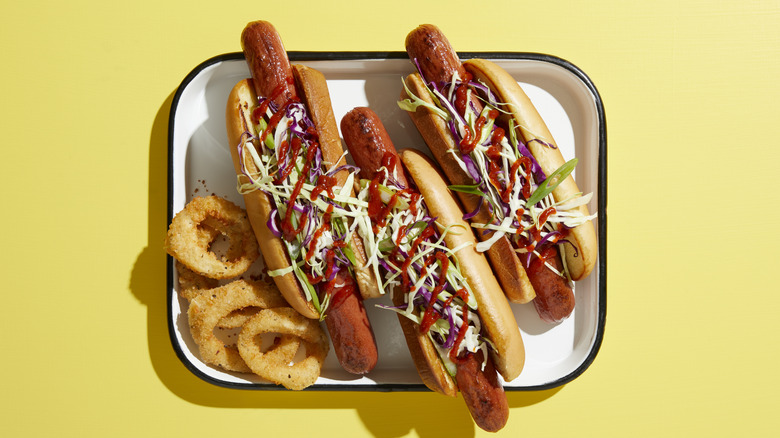 three hot dogs on a tray with a side of onion rings