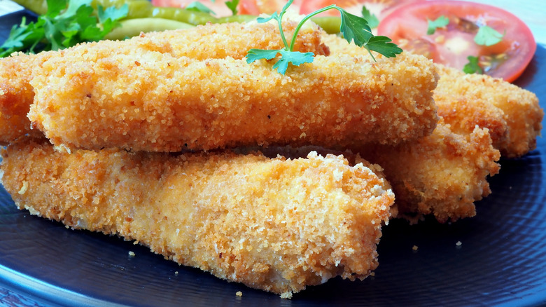 Crispy fish sticks on a black plate with an herb garnish