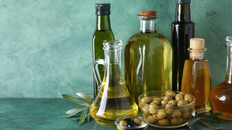 Different glassware of fresh olive oil on green background