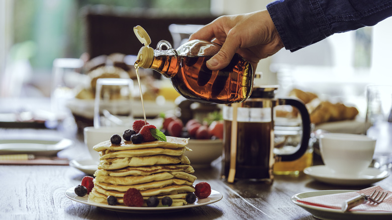 Maple syrup poured from glass bottle onto berry pancakes