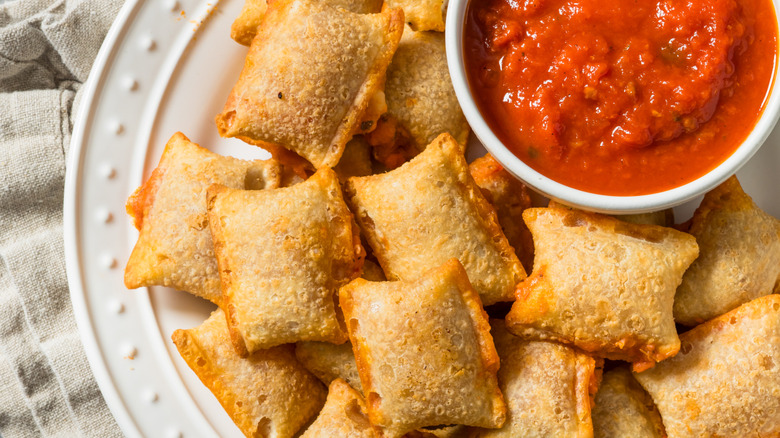 A plate of pizza rolls with a bowl of marinara sauce