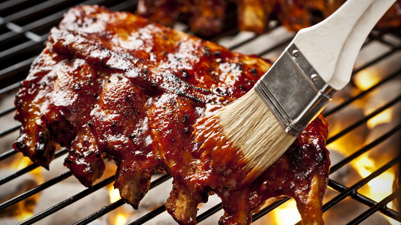 brushing bbq sauce onto ribs on grill
