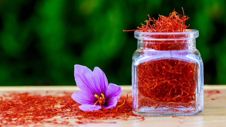 A jar of saffron next to a saffron flower