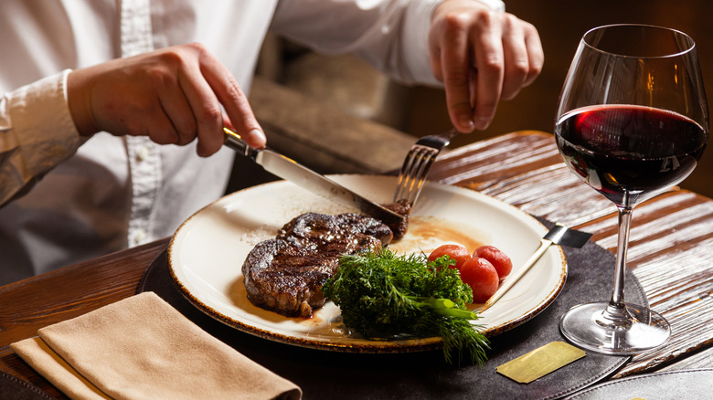 Person eating steak with glass of red wine