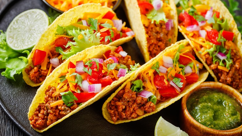 Crispy shelled tacos with ground beef, cheese, tomatoes and onions with limes and green salsa