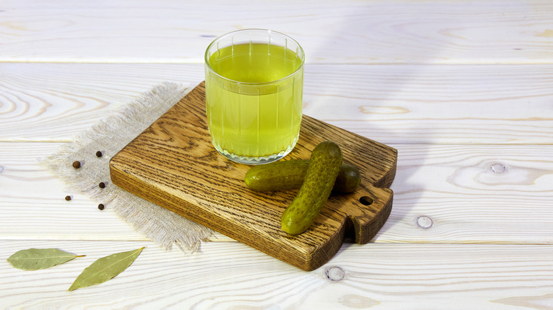 Glass of pickle brine next to pickles on a wooden board