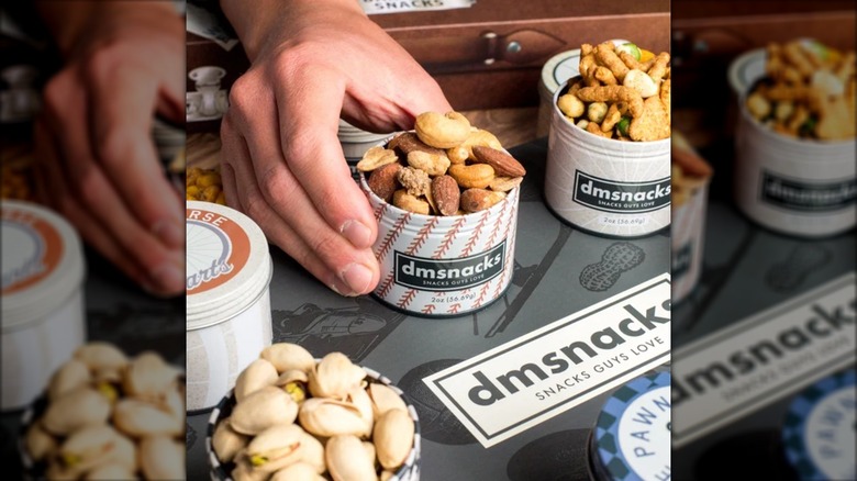 A hand grabs a tin of Damn Man Bar Cart snacks