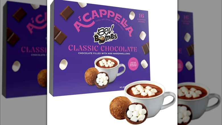 A package of A'cappella Classic Hot Chocolate BevBombs sits next to a bomb and a mug of cocoa