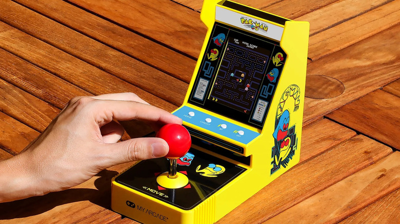 A hand plays a small Pac-Man arcade game