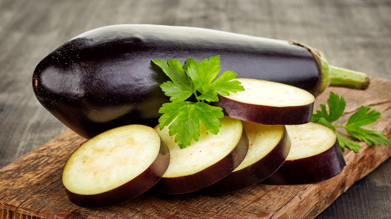 A whole eggplant and sliced eggplant on a wooden board