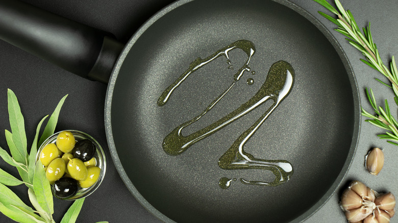 Oil in a frying pan, garlic, olives and rosemary on the side