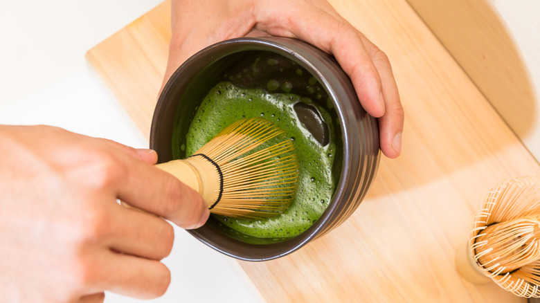 Matcha being whisked with water with a bamboo whisk in a bowl