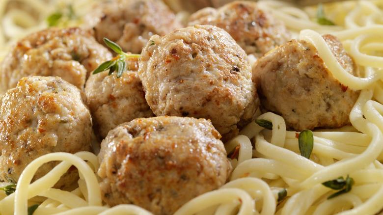 Turkey meatballs are nestled among spaghetti and fresh herbs