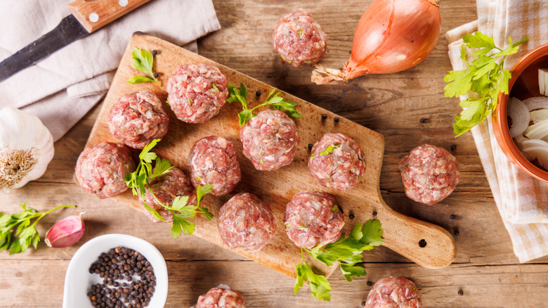 Raw meatballs with ingredients on cutting board