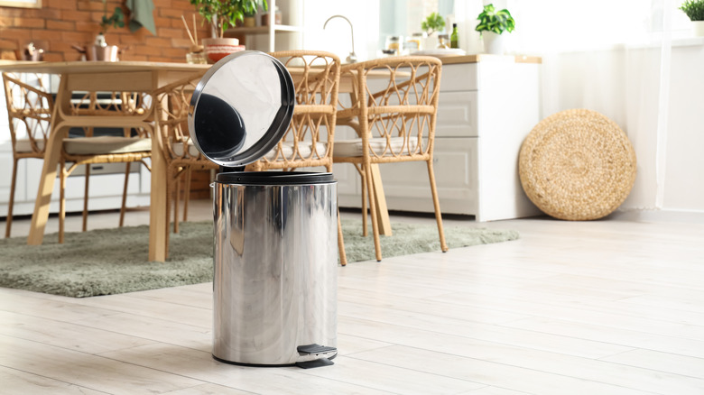The lid is open on a metal trash can off to the side of a kitchen.