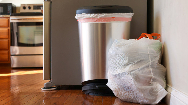 A full bag of trash sits next to a metal can in a kitchen