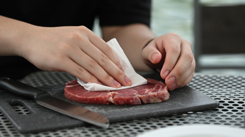 A hand patting a thin steak dry