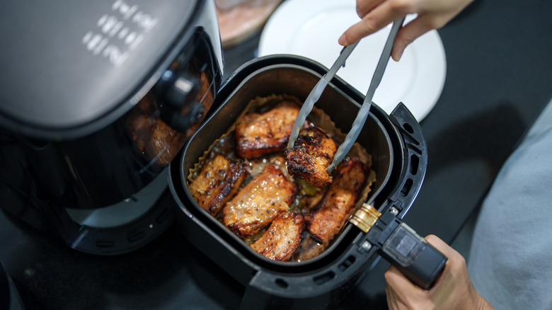 A person using plastic tongs to move cooking meat in the air fryer