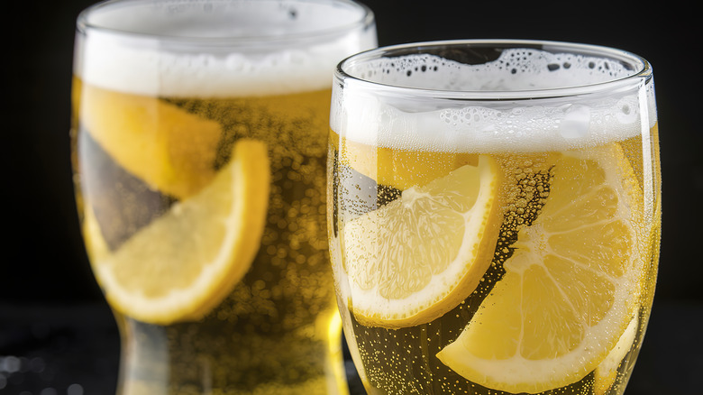Two glasses of cold beer with slices of citrus floating inside.
